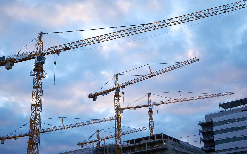 Lyftkranar framför några hus. Himlen har mörka moln.